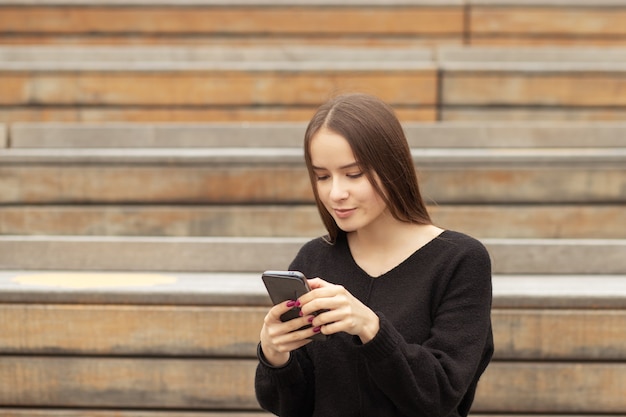 Jeune femme avec un téléphone dans la rue sur un banc sourit