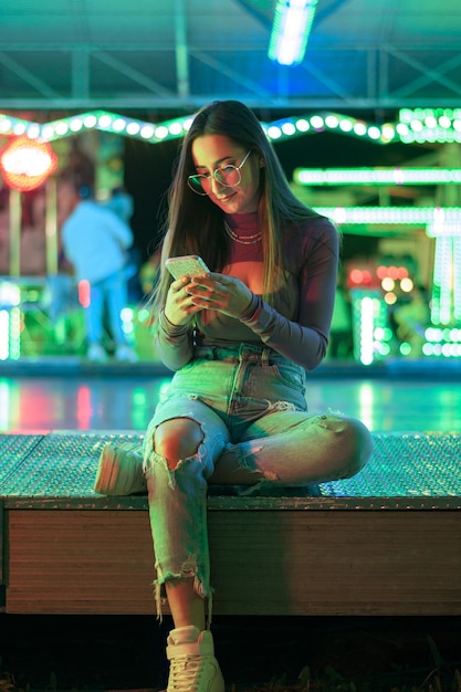 Jeune femme avec un téléphone éclairé par des lumières foraines