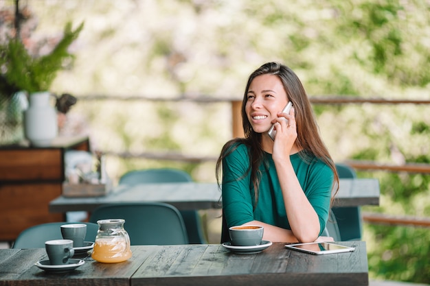 Jeune femme avec téléphone intelligent tout en étant assis seul dans un café pendant le temps libre