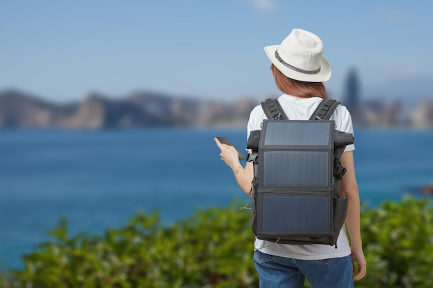 Jeune femme avec téléphone portable dans les mains et batterie solaire portable sur fond de rivière à l'extérieur