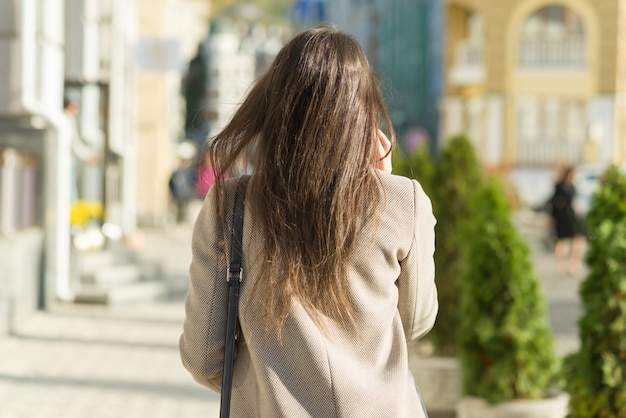 Jeune femme avec un téléphone portable marchant dans la rue ensoleillée