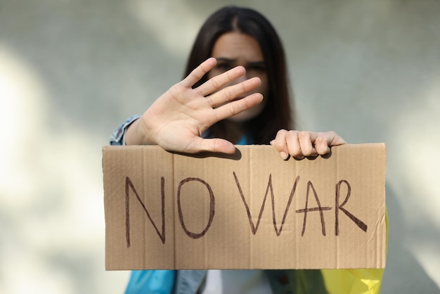 Jeune femme tenant une affiche avec des mots Pas de guerre et montrant un geste d'arrêt près du mur lumineux se concentrer sur la main