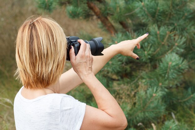 Jeune femme tenant un appareil photo numérique et prenant des photos du paysage d'été à forest