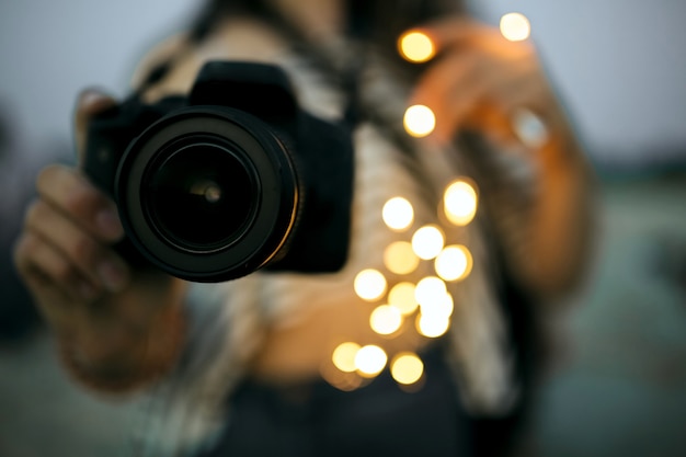 Photo jeune femme tenant un appareil photo numérique professionnel avec lumière bokeh