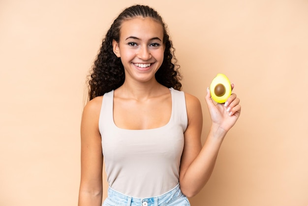 Jeune femme tenant un avocat isolé sur fond beige souriant beaucoup