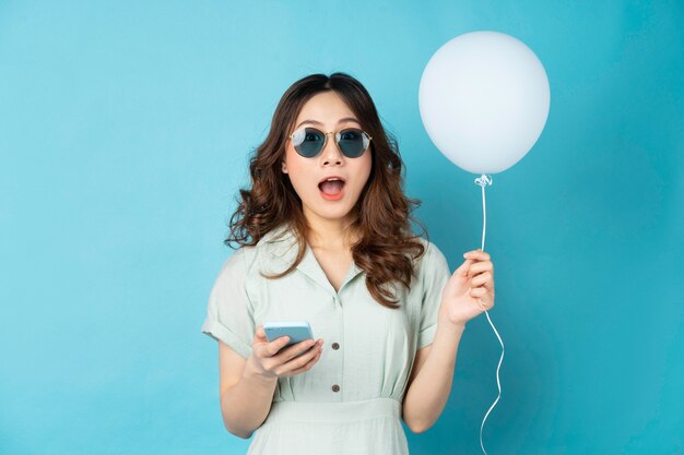 Jeune femme tenant des ballons et à l'aide de téléphone avec une expression surprise sur turquoise