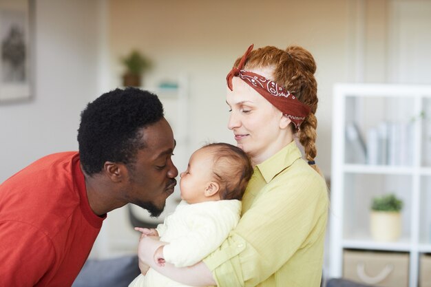 Jeune femme tenant bébé sur ses mains tandis que l'homme africain l'embrassant ils sont à la maison