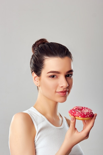 Jeune femme tenant un beignet dans un débardeur blanc sur fond blanc