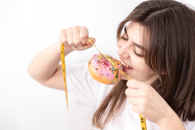 Jeune femme tenant un beignet avec un ruban à mesurer isolé