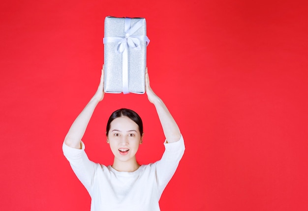 Jeune femme tenant une boîte-cadeau au-dessus de sa tête