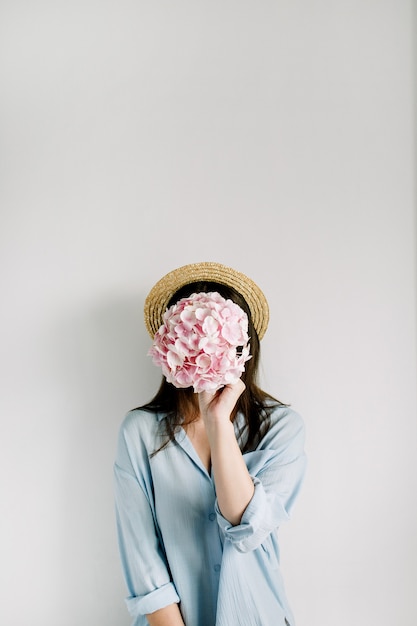 Jeune femme tenant un bouquet de fleurs d'hortensia rose sur une surface blanche