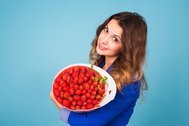 Jeune femme tenant un bouquet de fraises sur fond bleu