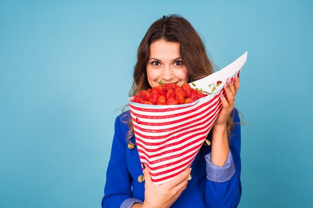 Jeune femme tenant un bouquet de fraises sur fond bleu