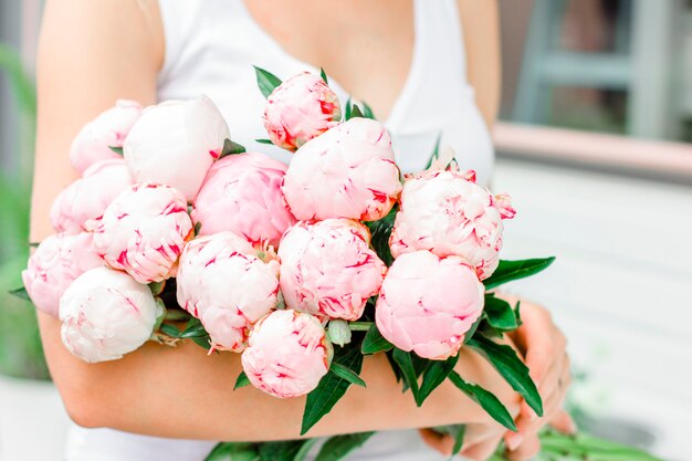 Photo jeune femme tenant un bouquet de pivoines roses blanches dans la rue