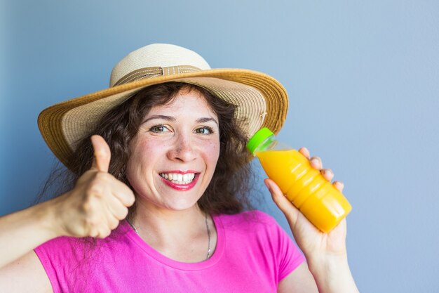 Jeune femme tenant une bouteille de jus et montrant le geste du pouce vers le haut.