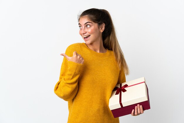 Jeune femme tenant un cadeau isolé sur blanc pointant vers le côté pour présenter un produit