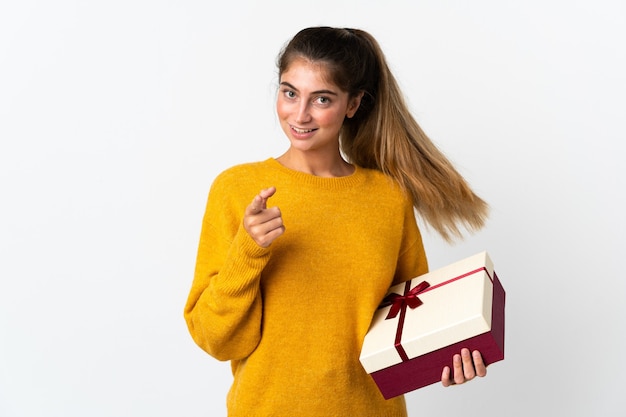 Jeune femme tenant un cadeau isolé sur blanc surpris et pointant vers l'avant