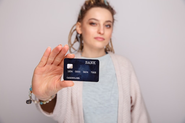 Jeune femme tenant une carte de crédit bleu foncé isolée sur fond gris.