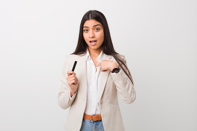 Jeune femme tenant une carte de crédit surprise pointant sur lui-même, souriant largement