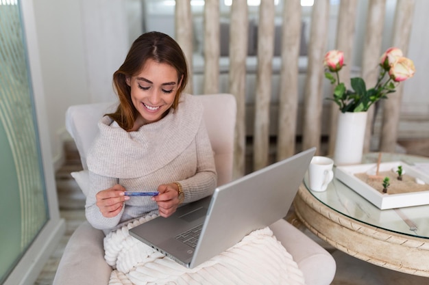 Jeune femme tenant une carte de crédit et utilisant un ordinateur portable. Concept d'achat en ligne. Femme heureuse faisant des achats en ligne à la maison