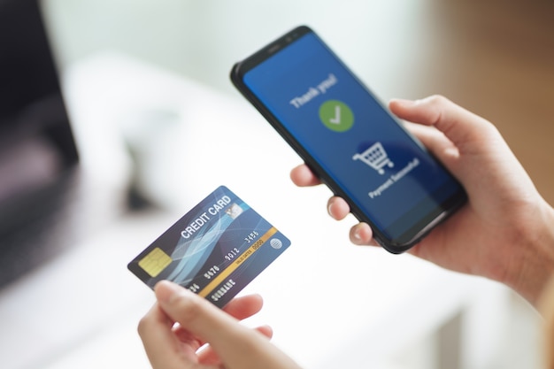 Jeune femme tenant une carte de crédit et utilisant un téléphone intelligent pour les achats en ligne, les services bancaires sur Internet, le commerce électronique, dépenser de l'argent, travailler à domicile