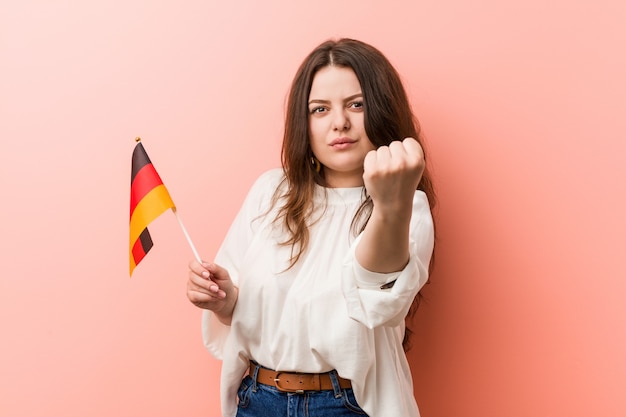 Jeune femme tenant un drapeau de l'Allemagne montrant le poing à la caméra, une expression faciale agressive.