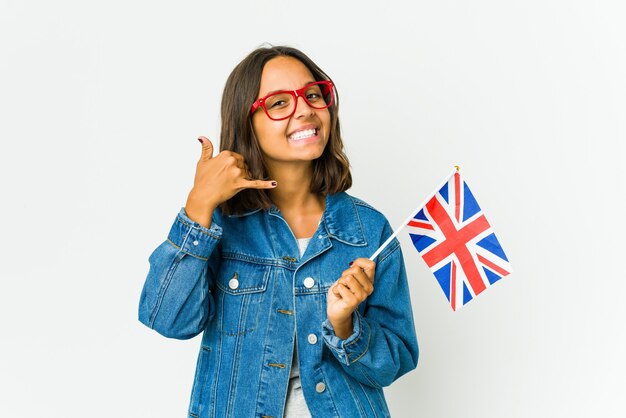 Jeune femme tenant un drapeau anglais isolé sur un mur blanc montrant un geste d'appel de téléphone mobile avec les doigts