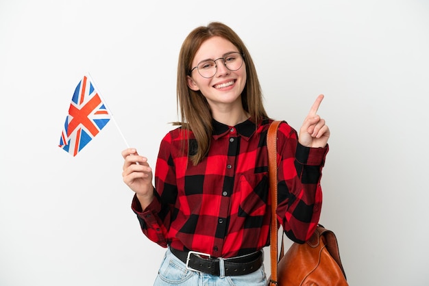 Jeune femme tenant un drapeau du Royaume-Uni isolé sur fond bleu montrant et levant un doigt en signe du meilleur