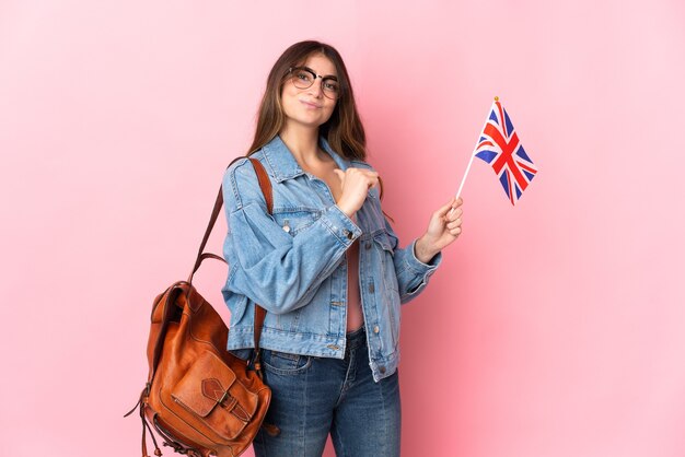 Jeune femme tenant un drapeau du Royaume-Uni isolé sur un mur rose fier et satisfait de soi