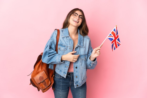 Jeune femme tenant un drapeau du Royaume-Uni isolé sur un mur rose souriant beaucoup