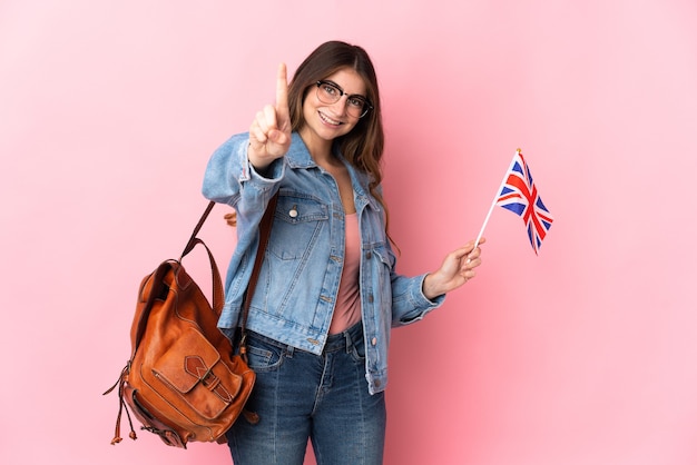 Jeune femme tenant un drapeau du Royaume-Uni isolé sur rose montrant et en soulevant un doigt