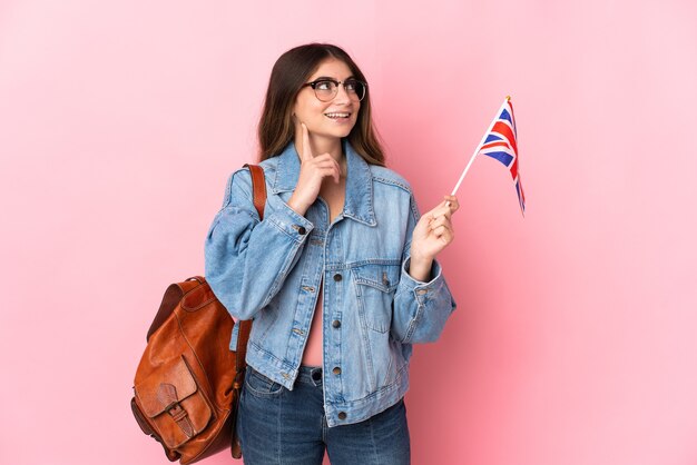 Jeune femme tenant un drapeau du Royaume-Uni isolé sur rose pensant une idée tout en levant