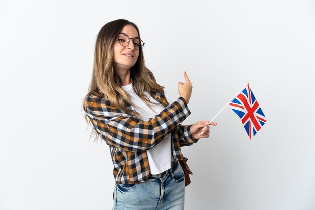 Jeune femme tenant un drapeau du Royaume-Uni posant isolé contre le mur blanc