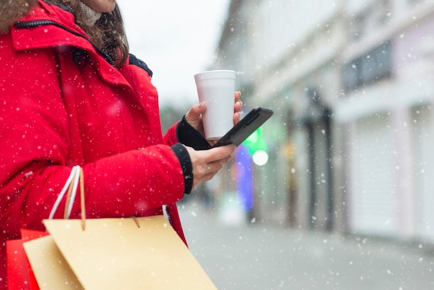 Jeune femme tenant du thé et utilisant un téléphone en plein air dans la rue d'hiver