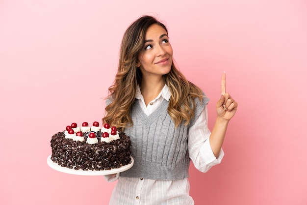 Jeune femme tenant un gâteau d'anniversaire sur fond rose isolé pointant vers une excellente idée