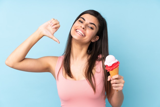 Jeune femme tenant une glace au cornet sur un mur bleu isolé fier et satisfait de soi