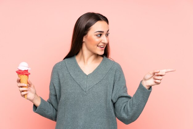 Jeune femme tenant une glace cornet isolée sur un mur rose pointant vers le côté pour présenter un produit