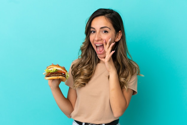 Jeune femme tenant un hamburger sur fond isolé criant avec la bouche grande ouverte