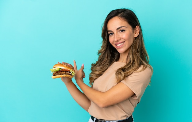 Photo jeune femme tenant un hamburger sur fond isolé pointant vers l'arrière