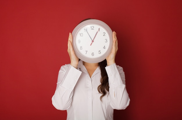 Jeune femme tenant une horloge sur un fond rouge.