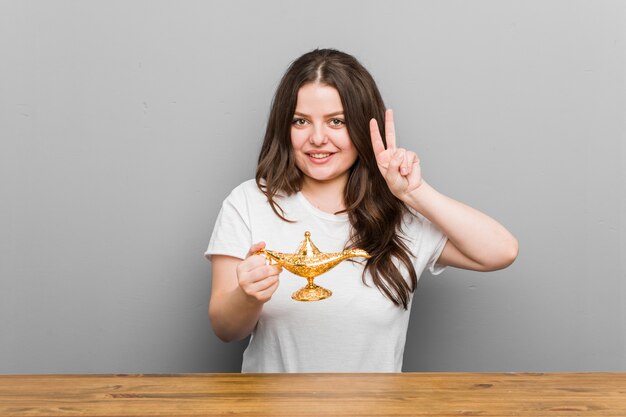 Jeune femme tenant une lampe magique montrant le signe de la victoire et souriant largement.