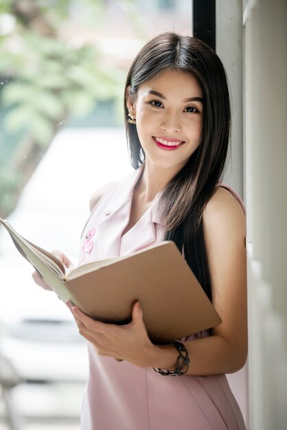 Jeune femme tenant un livre et regardant la caméra tout en restant à l&#39;extérieur.