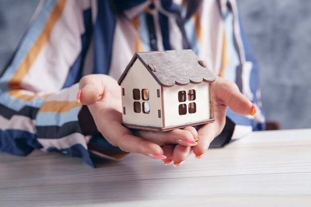 Jeune femme tenant une maison devant une table