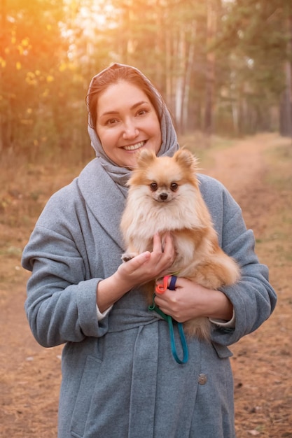 Jeune femme tenant un mini spitz poméranien dans les bras en marchant dans un parc d'automne