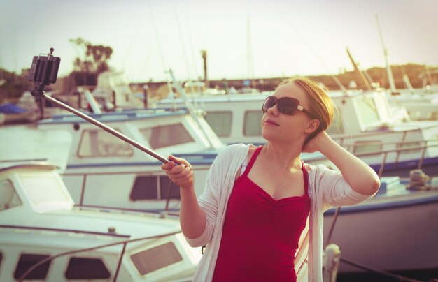 Photo une jeune femme tenant un monopode tout en prenant un selfie via un téléphone intelligent au port