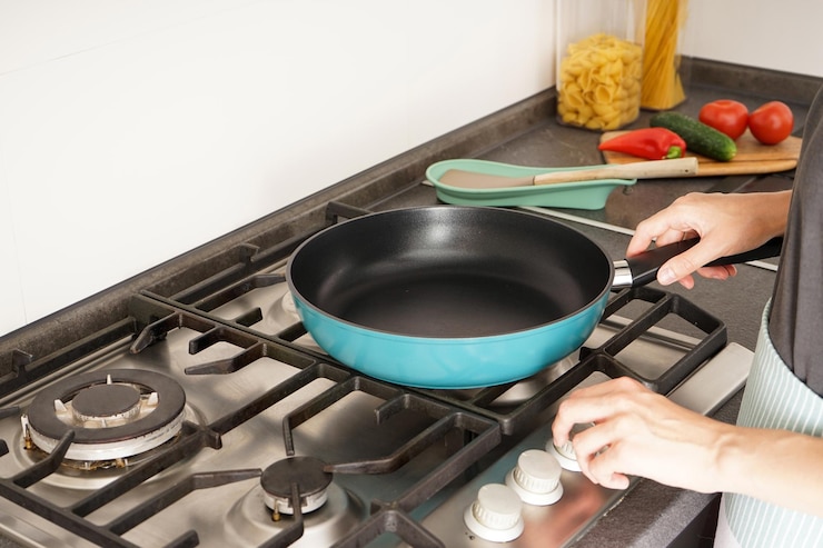 Photo jeune femme tenant une nouvelle poêle à frire dans ses mains sur le fond de la cuisine et des légumes