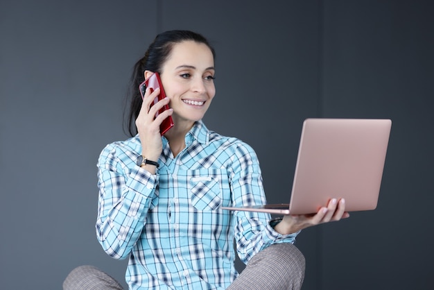 Jeune femme tenant un ordinateur portable dans ses mains et parler au téléphone. Concept de travail indépendant