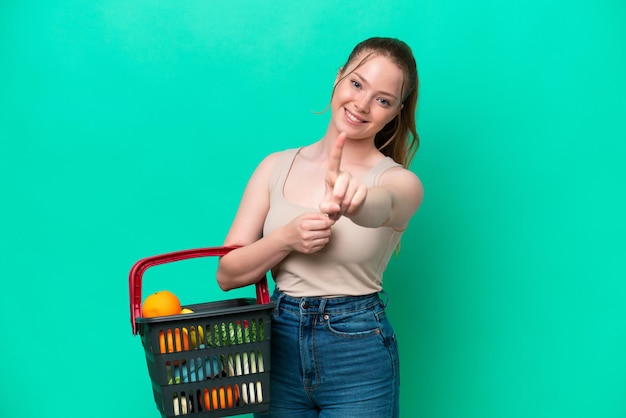 Jeune femme tenant un panier plein de nourriture isolé sur fond vert