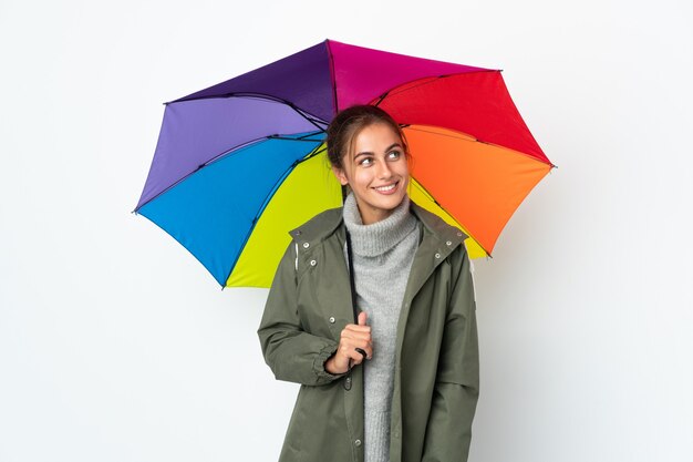 Jeune femme tenant un parapluie sur fond blanc pensant une idée tout en levant