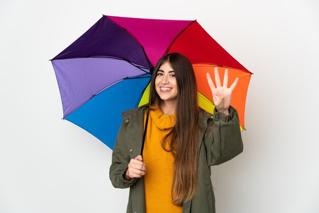 Jeune femme tenant un parapluie isolé sur fond blanc heureux et comptant quatre avec les doigts